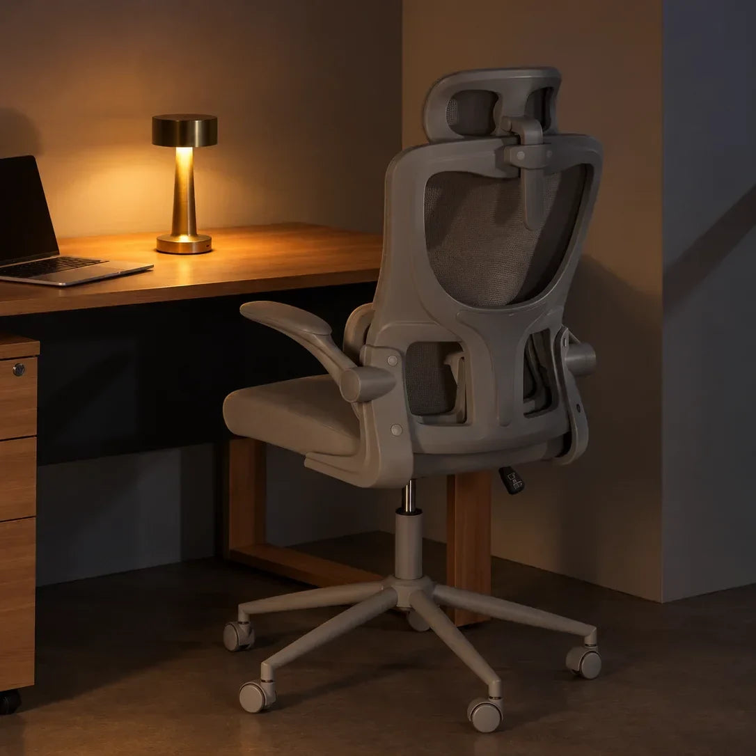 A brass table lamp glowing warmly on a desk beside a laptop, in a modern home office with an ergonomic chair, shown with the lamp fully in frame.